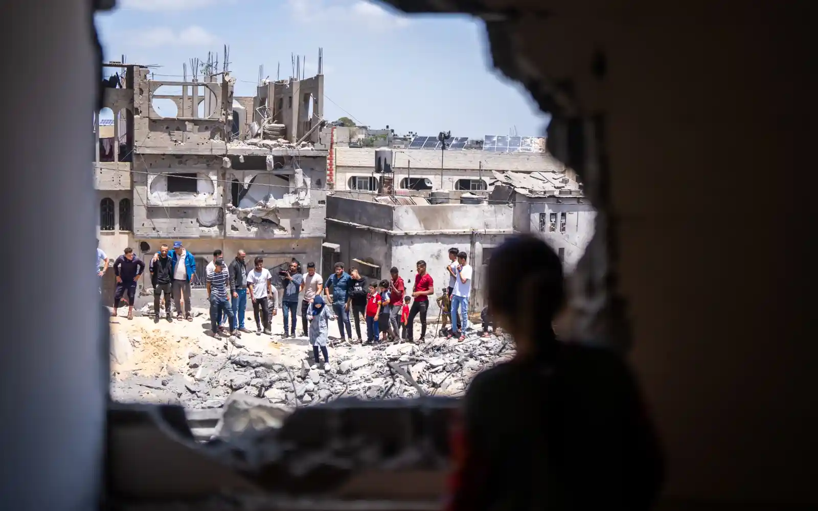 Un groupe de personnes examine les dommages subis par une zone résidentielle dans la bande de Gaza. ©OMS