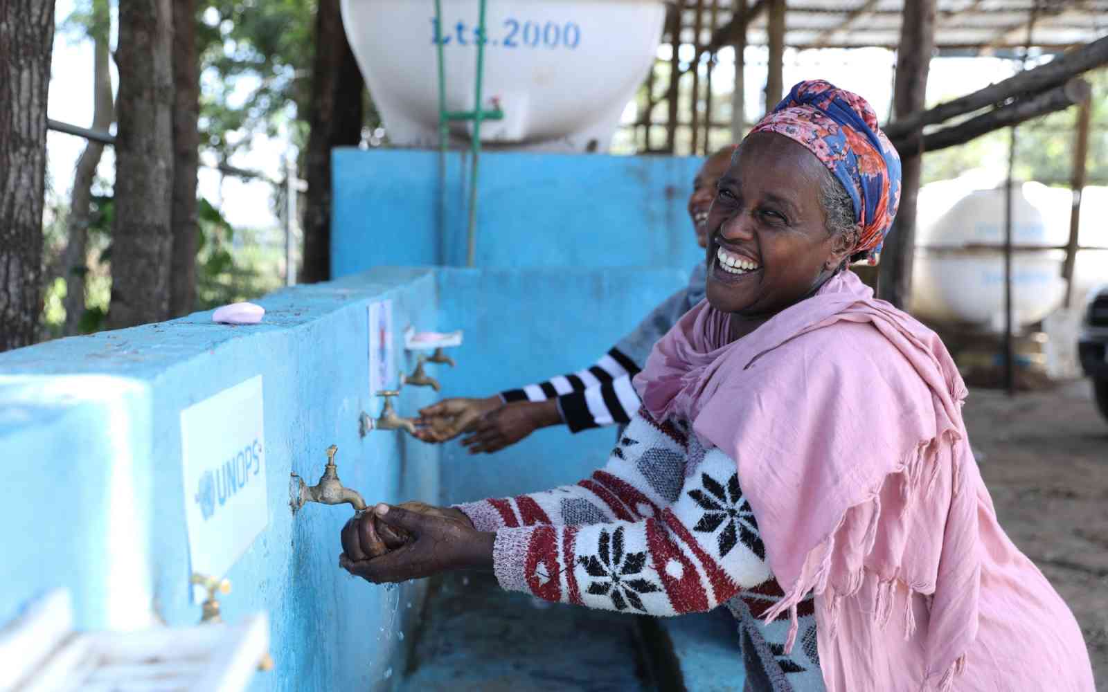 A woman washes her hands at a row of outdoor taps.