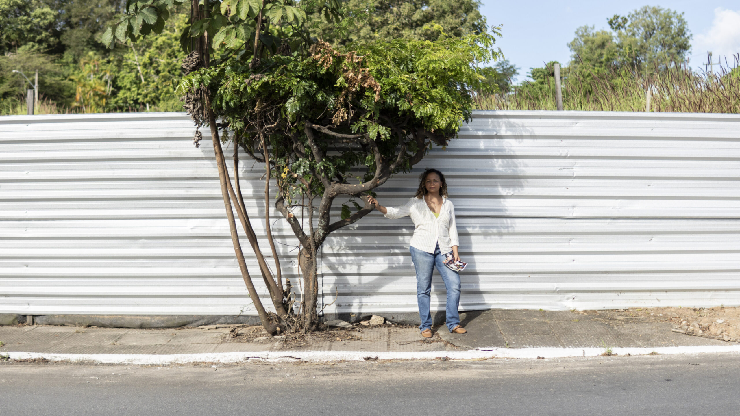 Roberta Santos parada na frente da árvore plantada pela sua família - a única coisa que sobrou do lugar onde estava sua casa