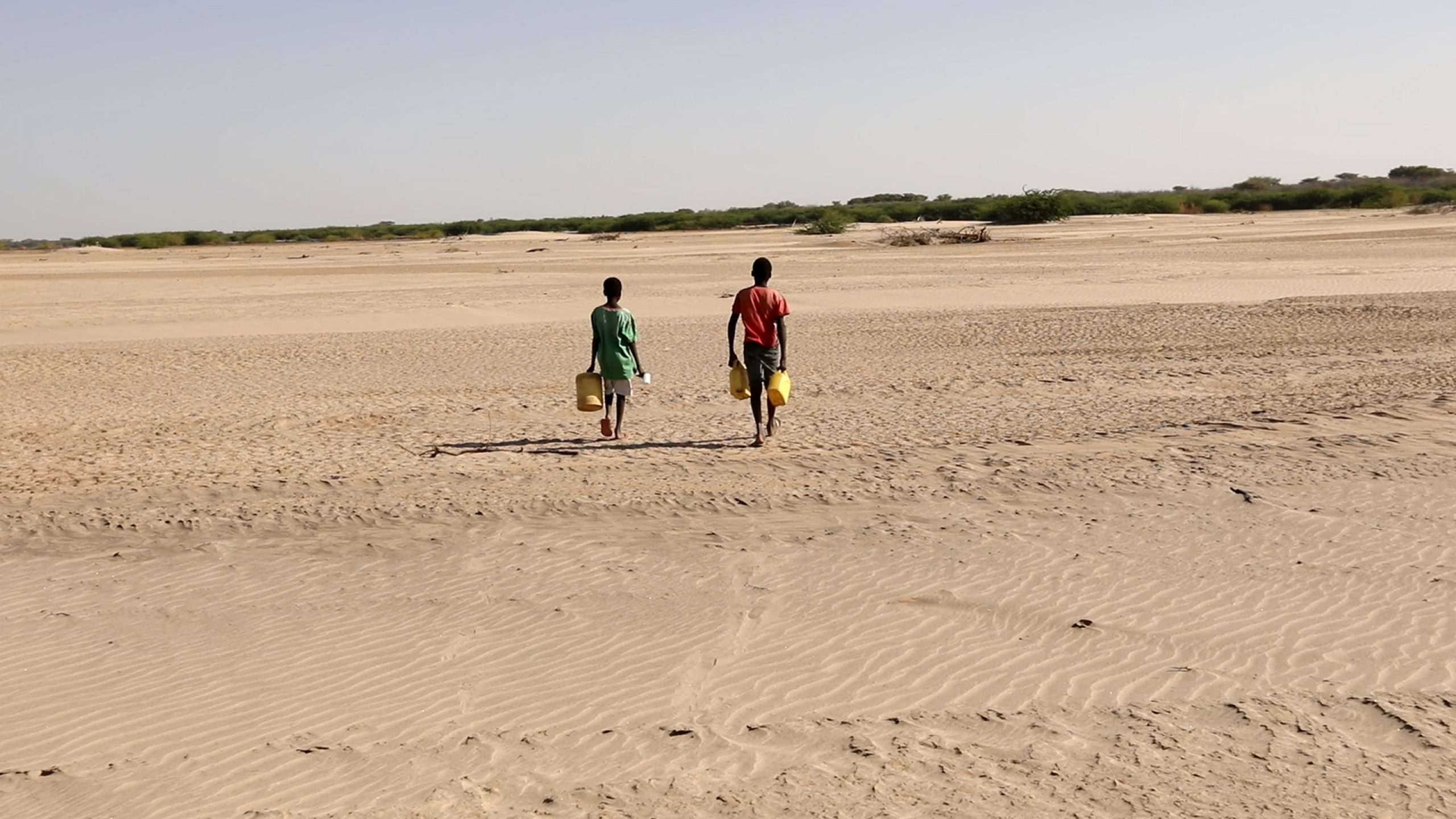 Les garçons s’arrêtent pour creuser un trou dans le lit de la rivière asséché et fissuré avec des pelles improvisées.