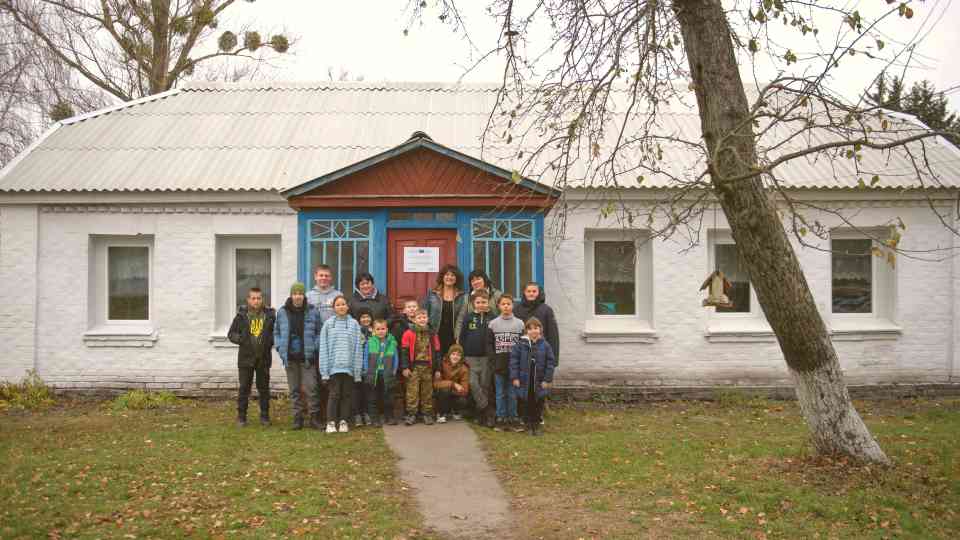 Students with their teacher standing in front of the renovated Pisky Secondary School. ©UNOPS/Veronika Yaresko