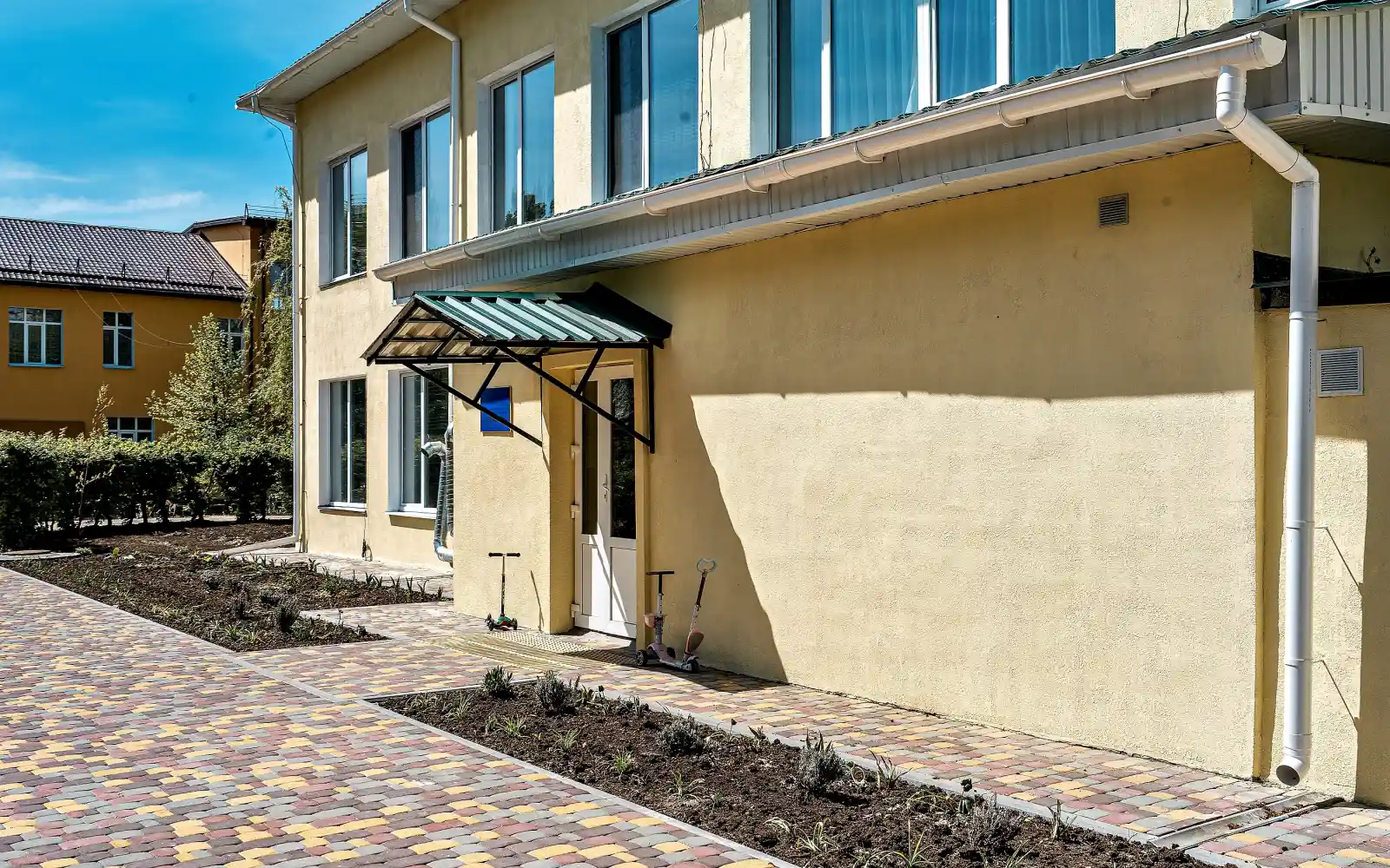 After;The preschool's facade and entrance are fully restored with a new paved walkway and freshly planted garden beds, creating a safe and welcoming environment.