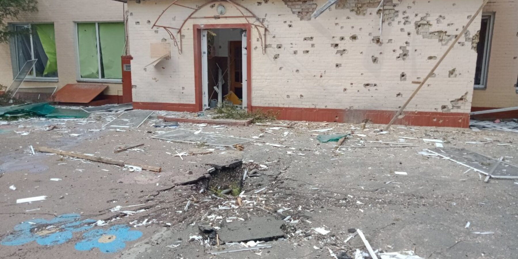 La fachada del centro preescolar y sus alrededores tras el impacto de un misil el 2 de marzo de 2022, con graves daños y escombros.
