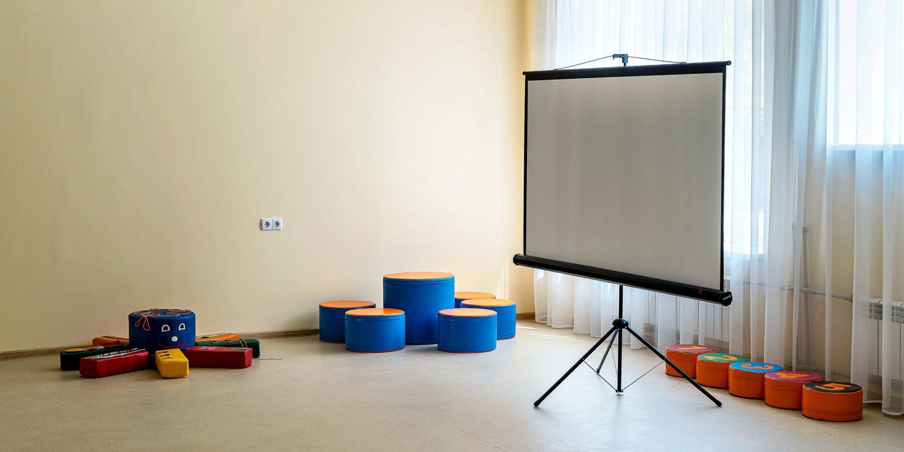 Una moderna sala multiusos equipada con nuevos asientos de colores y una pantalla de proyección ofrece un espacio luminoso para aprender y llevar a cabo actividades interactivas.