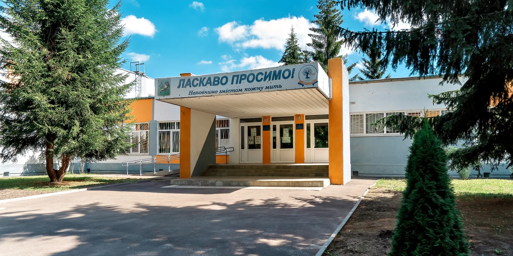 The main entrance to the school, with a canopy under the "Welcome" sign, is riddled with shrapnel damage.
