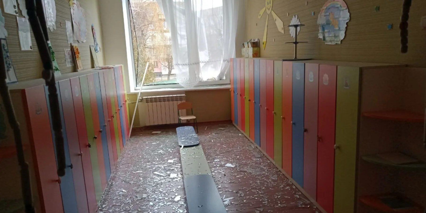 A classroom inside the preschool, with shattered glass on the floor and damaged furniture, following the missile blast.
