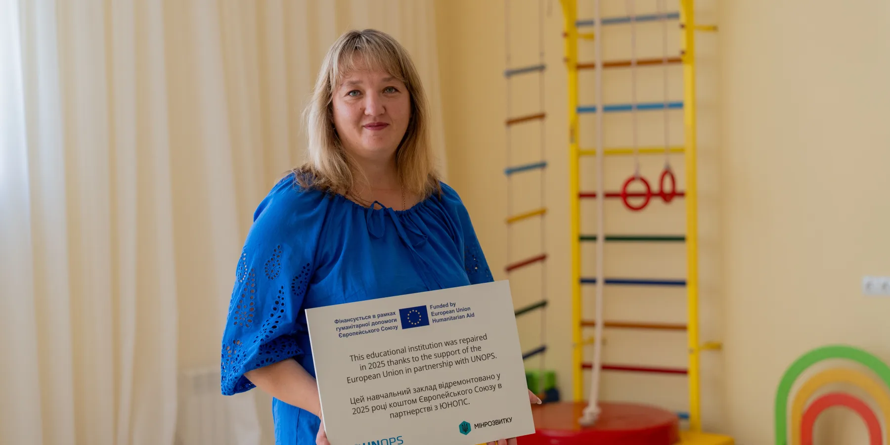 Oksana Petruk, Head of the Preschool Institution, holds a sign acknowledging the vital support from the European Union and UNOPS that made the school's renovation possible.