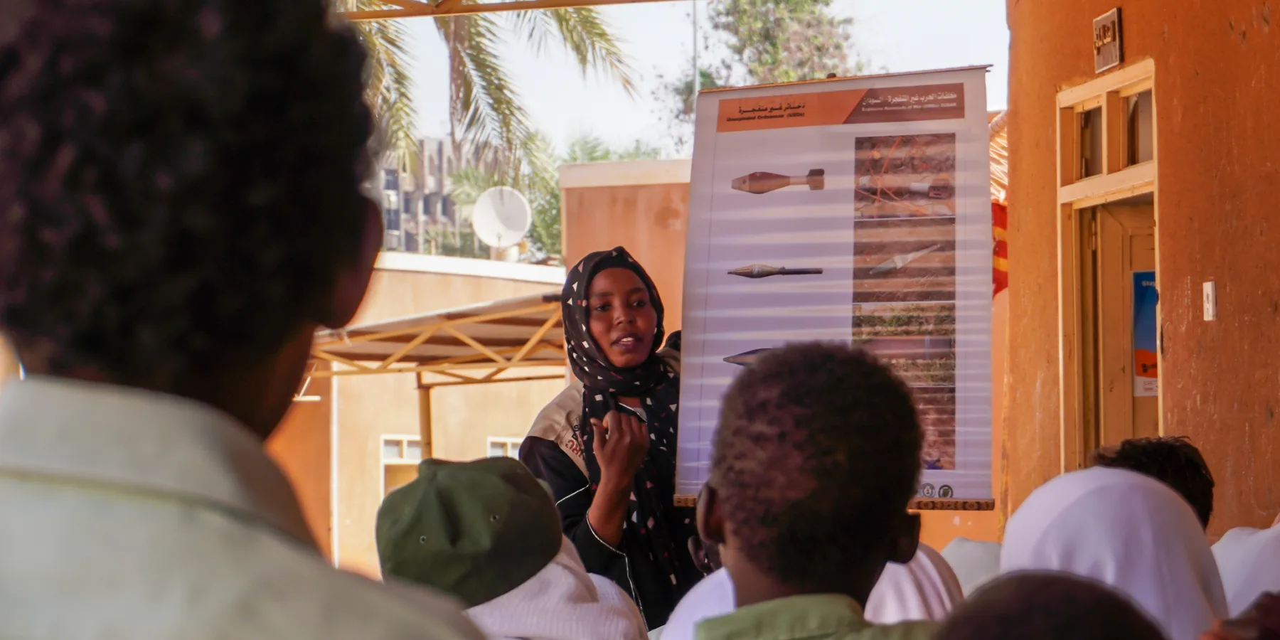 Nariman Dafallah Ibrahim Doka, punto focal de enlace comunitario de JASMAR, utiliza un cartel para mostrar distintos tipos de riesgos de explosivos durante una sesión de concientización para niños y niñas en Jartum.