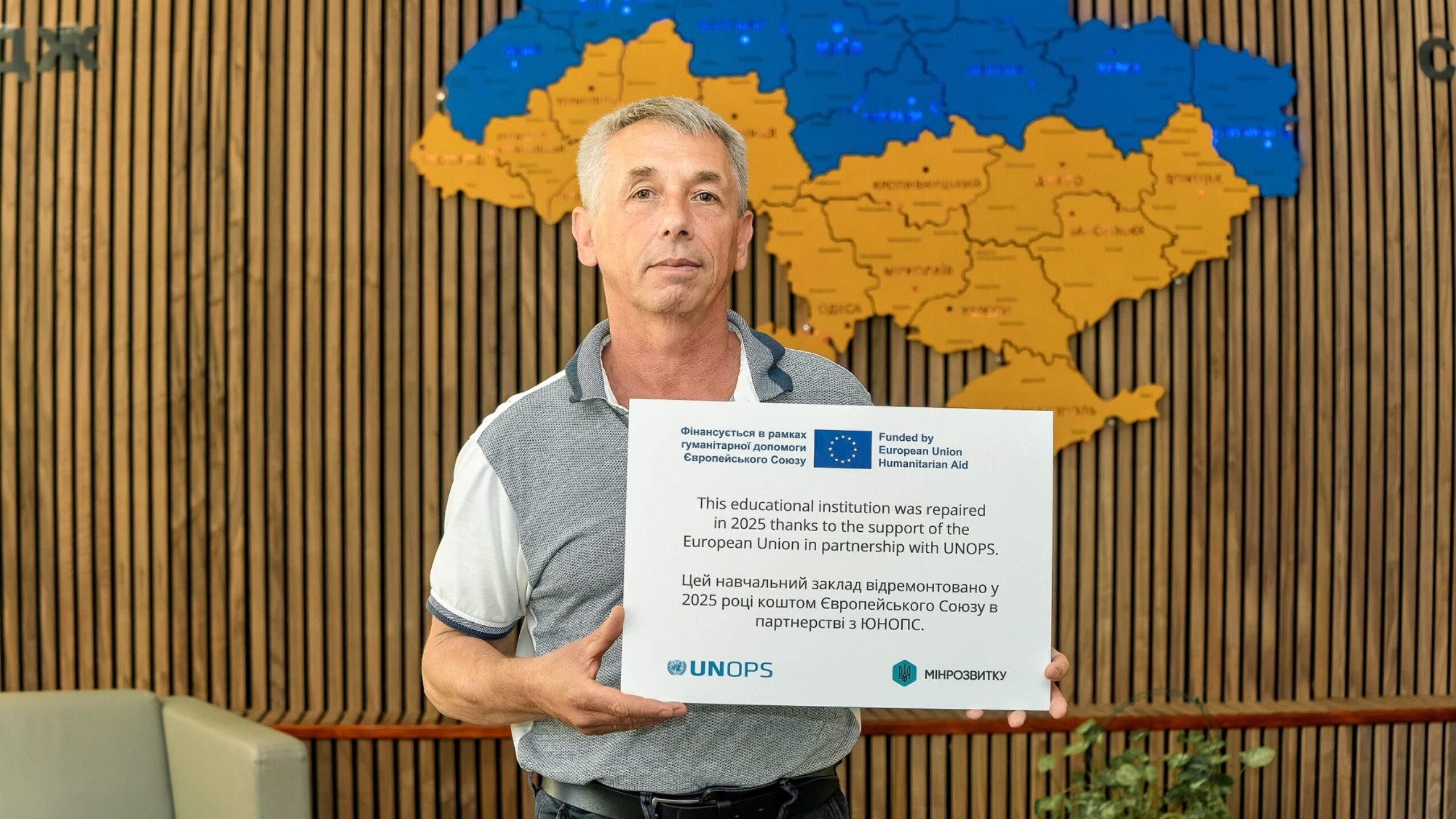 Yurii Aleksandrov, Instructor Sénior del Departamento de Mecanización y Transporte, sostiene una placa conmemorativa entregada a la escuela tras la finalización de las obras de rehabilitación. La placa reconoce el apoyo de la Unión Europea y UNOPS en las obras de 2025.
