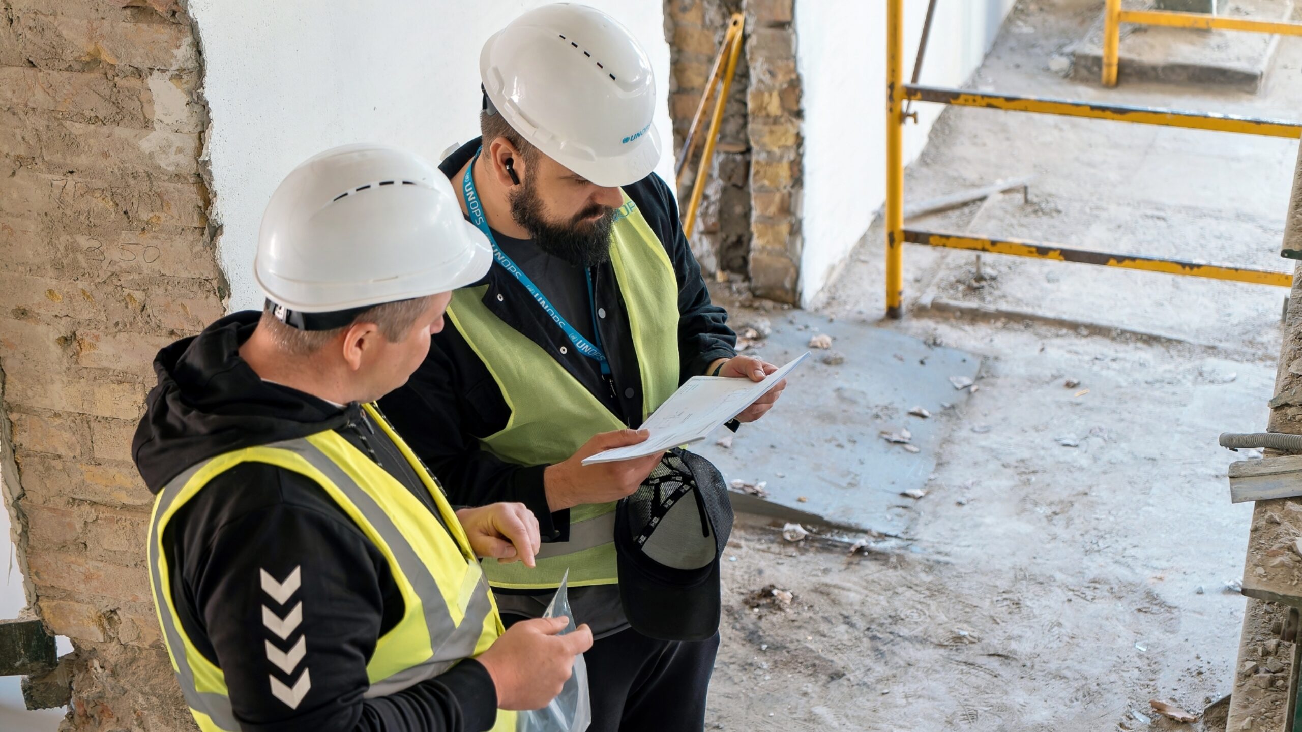 Un ingeniero de UNOPS y un representante del contratista examinan los planes in situ durante las obras de rehabilitación de la escuela de formación profesional de Katyuzhanka.