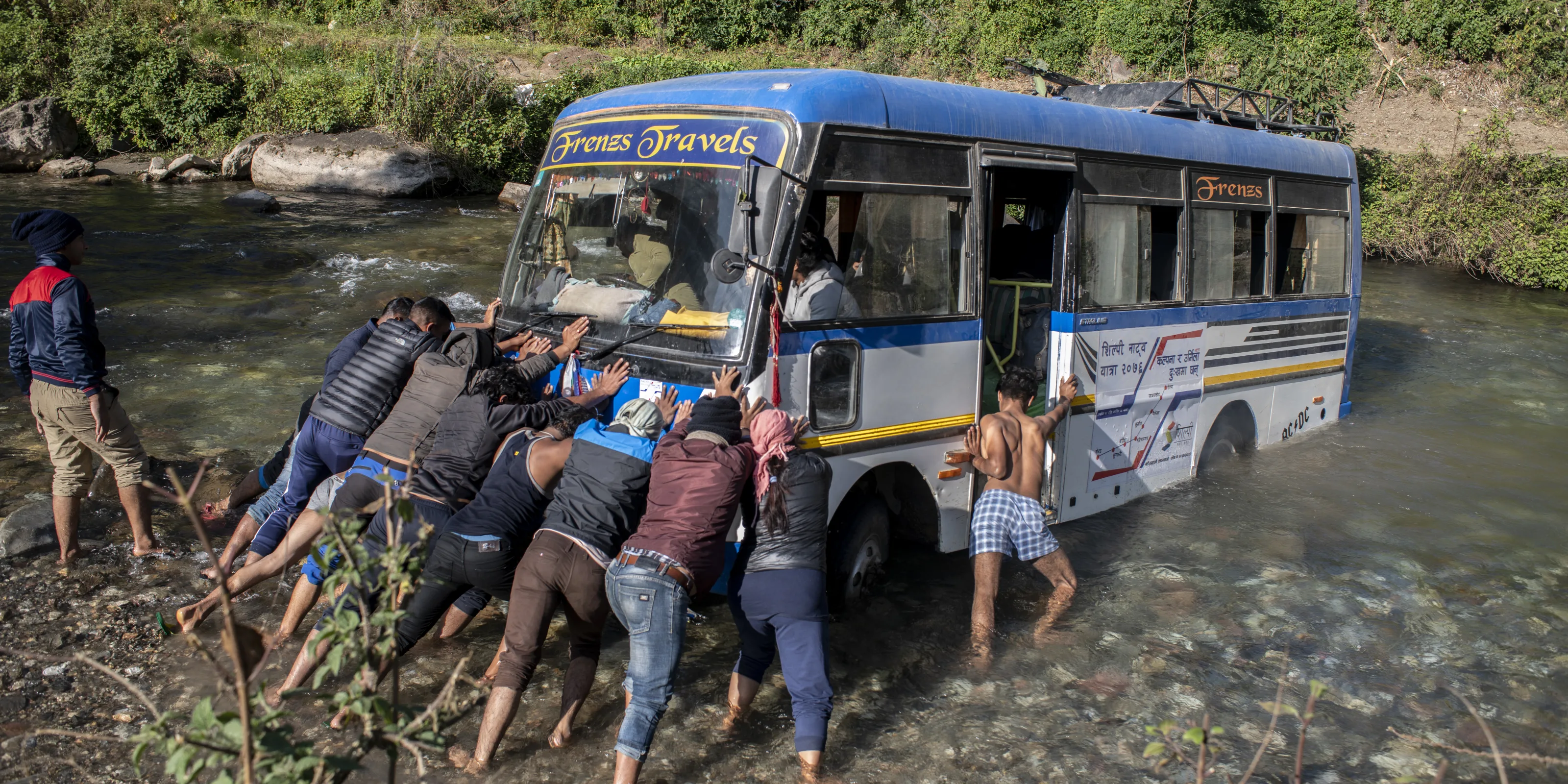 Members of the theatre group and villagers help dislodge the group’s minibus from the riverbed.