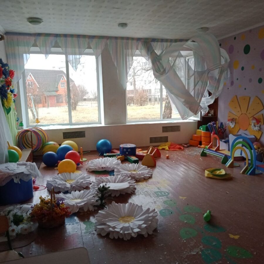 Otra vista de un aula dañada, con escombros esparcidos por el suelo y ventanas rotas.