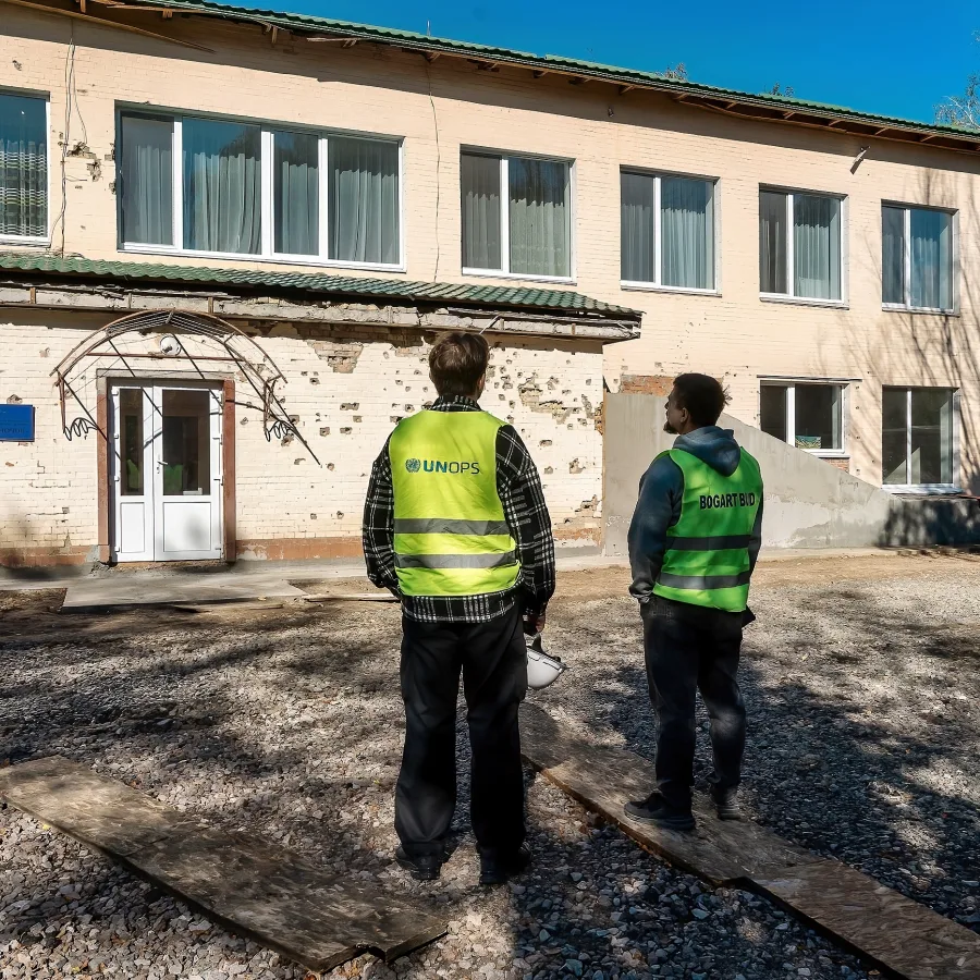 UNOPS and contractor personnel survey the damage to the preschool's exterior, planning the extensive repairs needed to make the building safe again.
