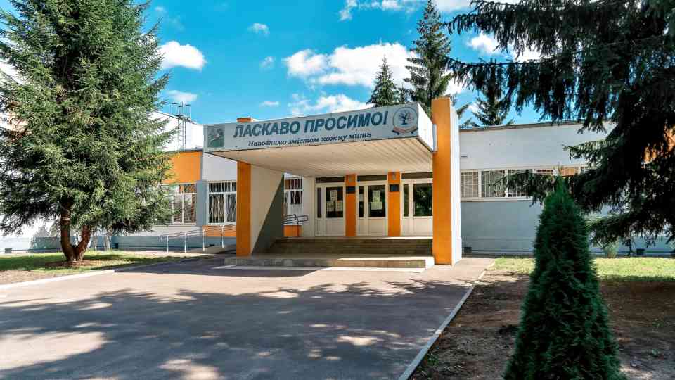The main entrance to the school, with a canopy under the "Welcome" sign, is riddled with shrapnel damage.